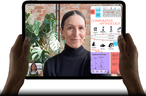 iPad Pro, face avant, orientation paysage, noir sidéral, angles arrondis, cadre noir de l’écran, mains tenant les côtés gauche et droit, écran affichant une conversation FaceTime en cours de traduction en direct, et une app éducative montrant une présentation de la mythologie comparée avec du texte, des diagrammes et des notes manuscrites